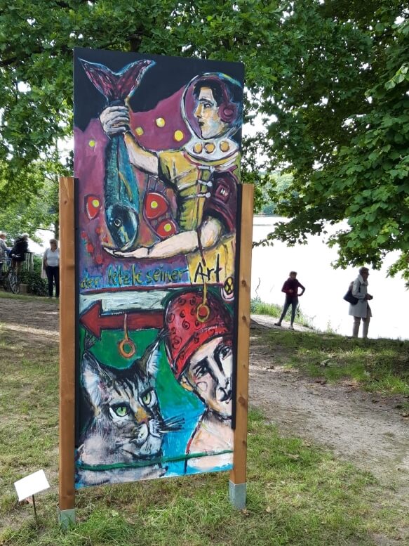 Ein Kunstwerk, das auf einer Staffelei in einem sommerlichen Garten ausgestellt ist.